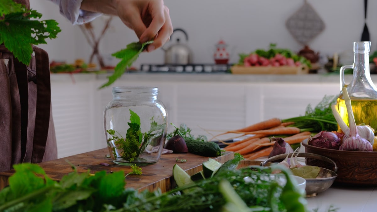Hand preparing herbs and vegetables in a kitchen setting. Fresh ingredients on a rustic table.
